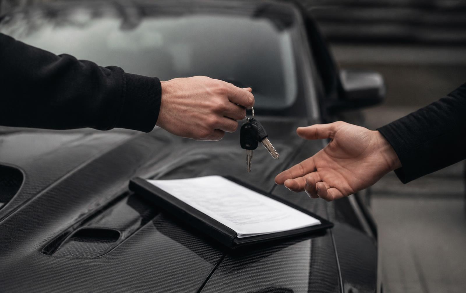 Keys and a document folder changing hands over the hood of a dark car