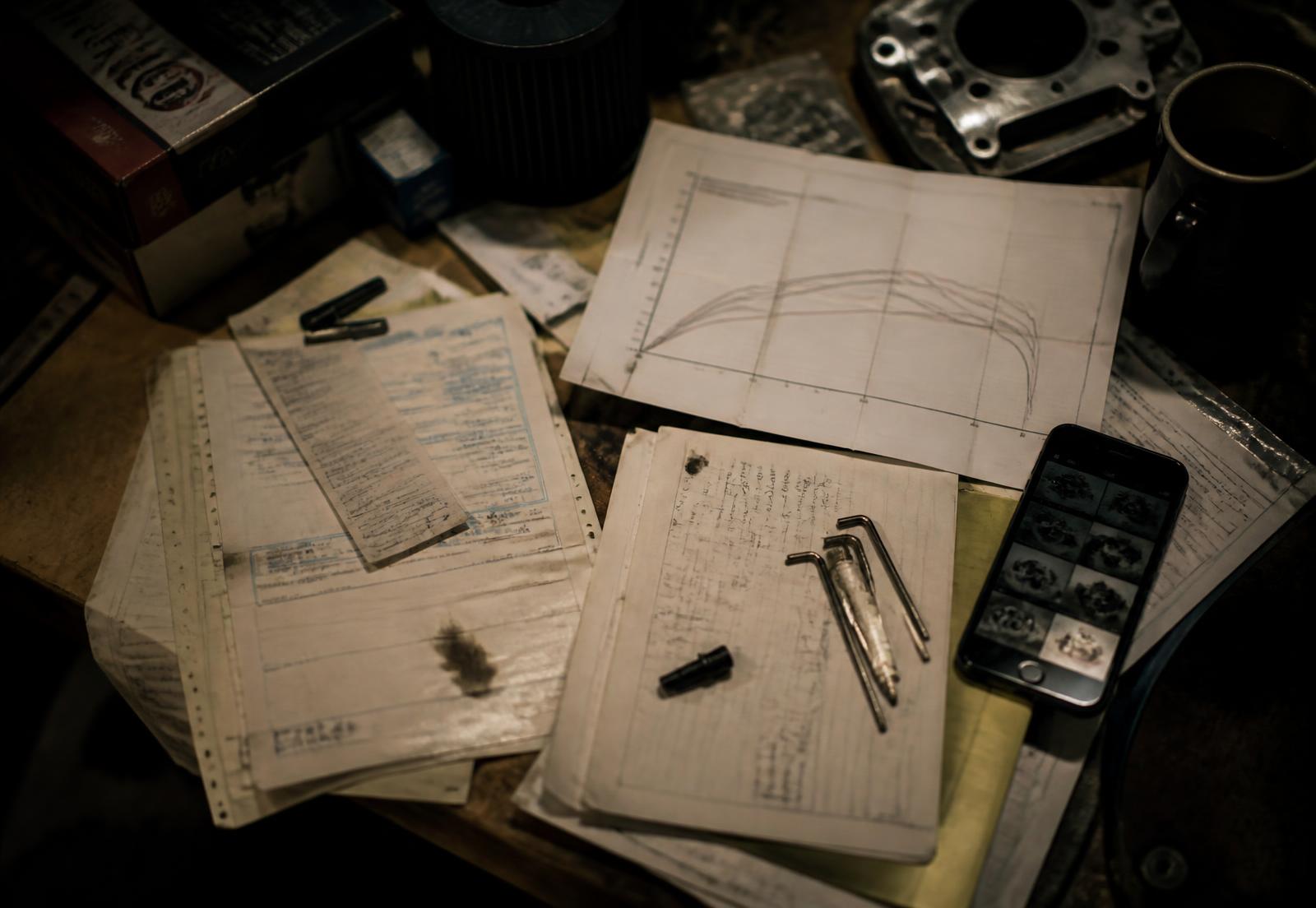 Invoices, a dyno printout, handwritten shop notes and a phone on a workbench